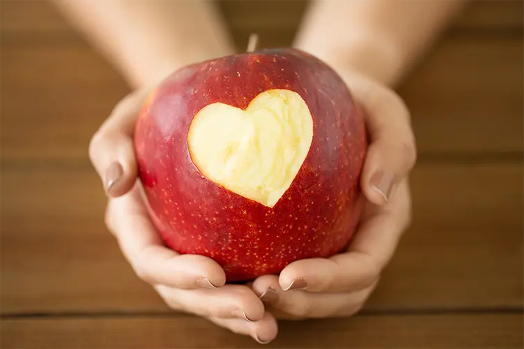 Närbild på händer som håller ett äpple där ett hjärta är utskuret.
