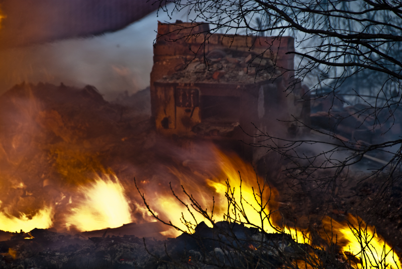 Brand i terräng ett uppbränt hus i bakgrunden