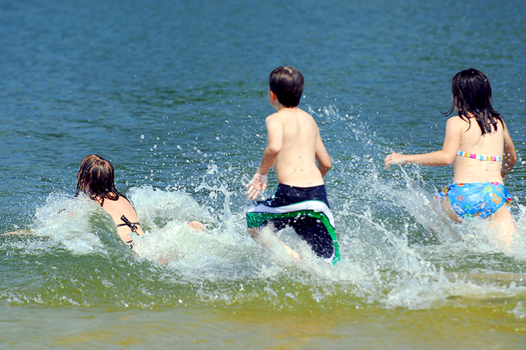 Tre barn springer ut i sjön för att bada.