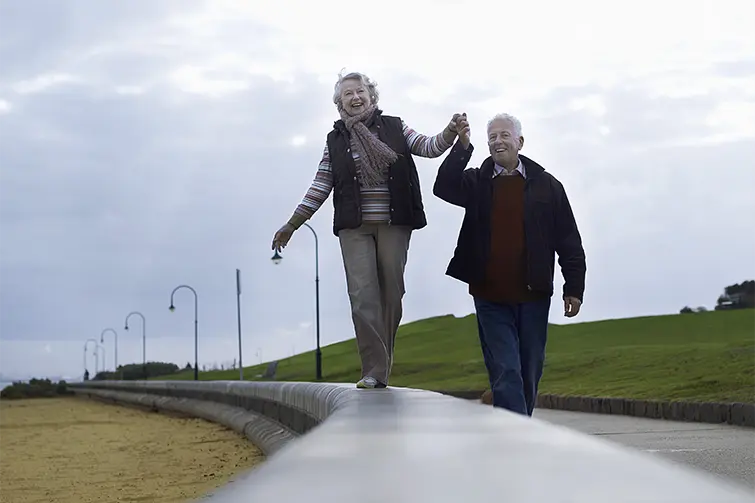 Äldre dam går balansgång och håller äldre herre i handen.