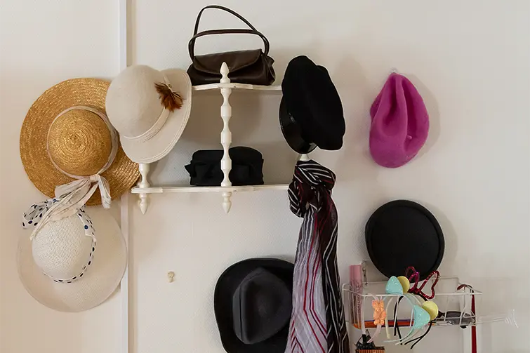Hattar som hänger på en vägg och väskor som står i en hylla.