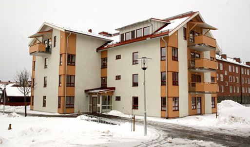 Hyreshuset Mangeln. Tre våningar + vindsvånig. Huset är beige och tegelröd. Vinterbild med snö.