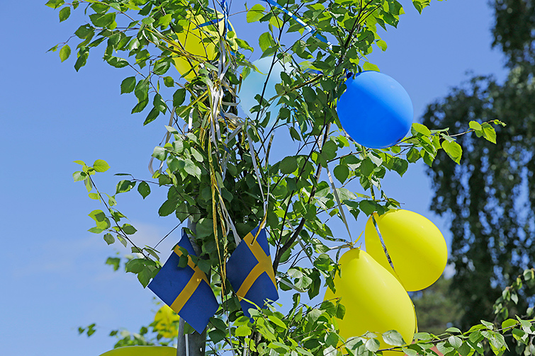 Närbild på trädgren som är pyntad med flaggor och ballonger.