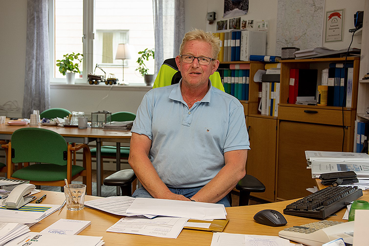 Lars-Olov syns i halvfigur sittandes i kontorsmiljö med papper och pärmar med mera.