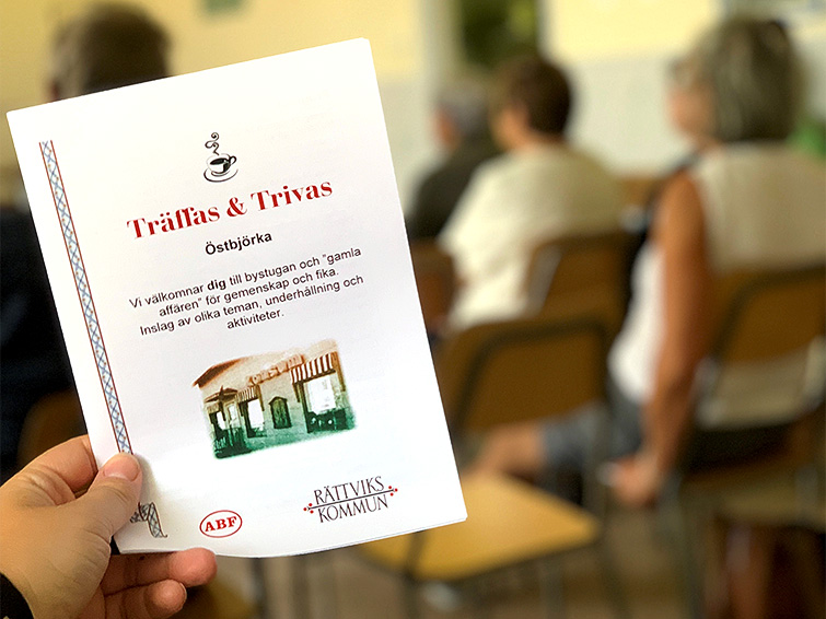 Programblad för Träffas och Trivas i Östbjörka samt deltagare i bakgrunden.