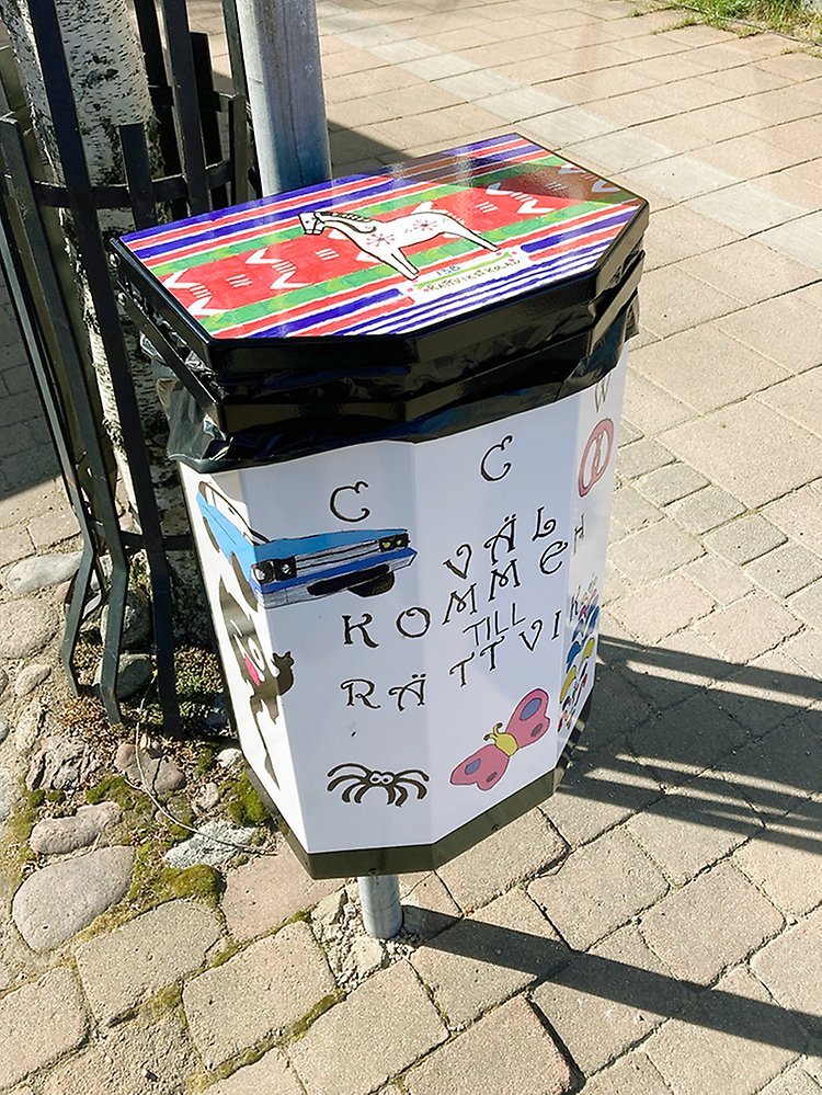 Målad papperskorg med texten "CCW, Välkommen till Rättvik" på Storgatan. 