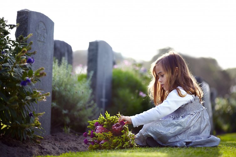 Liten flicka sitter framför grav.