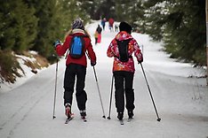 Två ungdomar med ryggsäckar åker längdskidor i skogen.