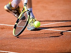 Man ser fötter, tennisracket och tennisboll på en som spelar tennis.