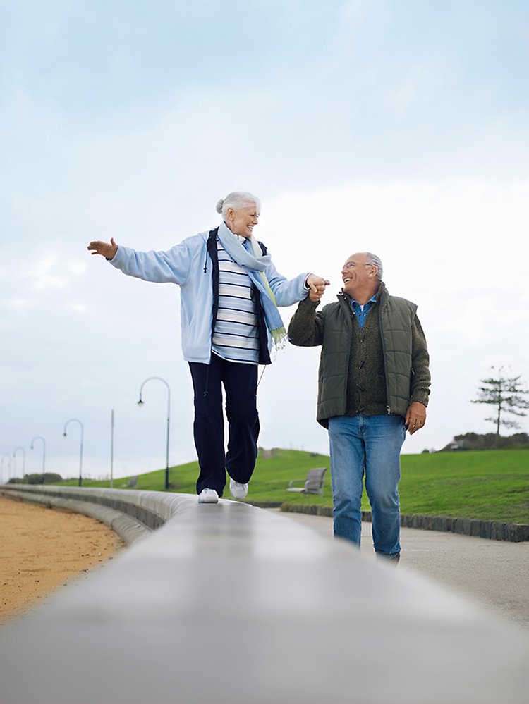 Äldre dam som går balansgång och håller äldre herre i handen.