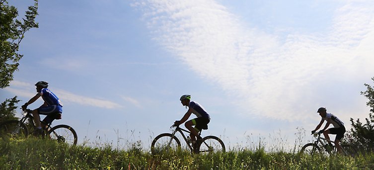 Tre cyklister, i bakgrunden klarblå himmel.